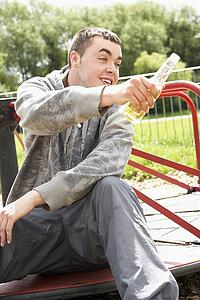 Young Man Sitting In Playground Drinking Beer