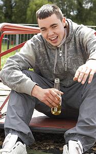 Young Man Sitting In Playground Drinking Beer