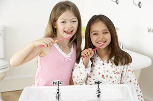 Two Young Girls Brushing Teeth at Sink