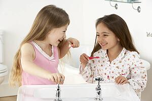 Two Young Girls Brushing Teeth at Sink