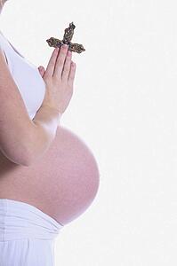Pregnant woman praying with a cross in her hands