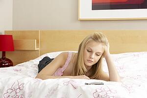 Sad Teenage Girl In Bedroom With Mobile Phone
