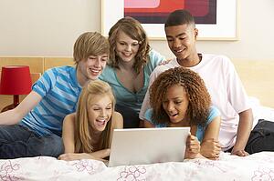 Group Of Five Teenage Using Laptop In Bedroom