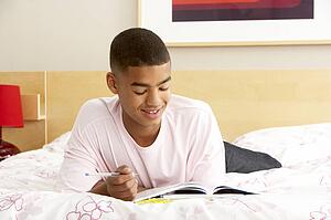 Teenage Boy Writing In Diary In Bedroom