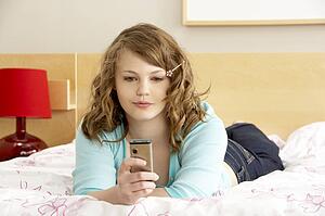Teenage Girl In Bedroom With Mobile Phone