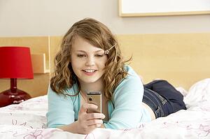 Teenage Girl In Bedroom With Mobile Phone