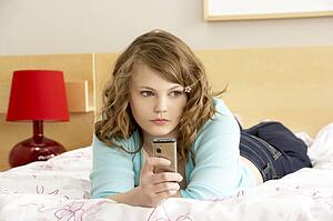 Sad Teenage Girl In Bedroom With Mobile Phone