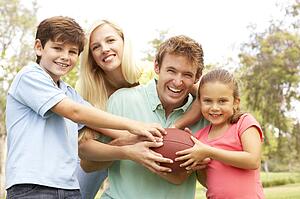 Family Playing American Football Together In Park