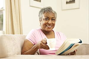 Senior Woman Reading Book With Drink At Home