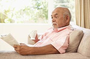 Senior Man Reading Book With Drink At Home