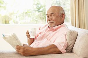 Senior Man Reading Book With Drink At Home