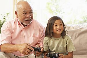 Grandfather And Granddaughter Playing Computer Game At Home