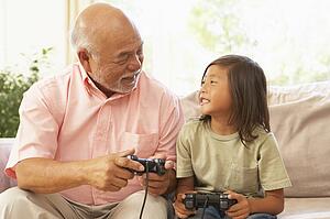 Grandfather And Granddaughter Playing Computer Game At Home