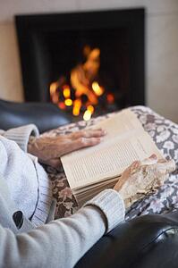 Detail Of Senior Woman Reading Book By Fire At Home