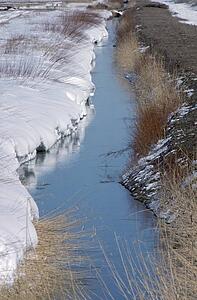 Irrigation ditch with snow drift on one side reflects sky, New Mexico, USA