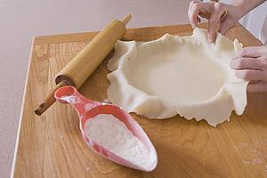 covering pie pan with dough on a cutting board with rolling pin and flour