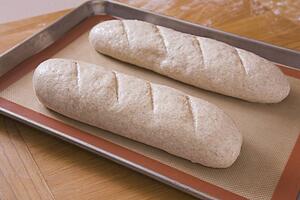 two uncooked loaves of bread on a baking sheet