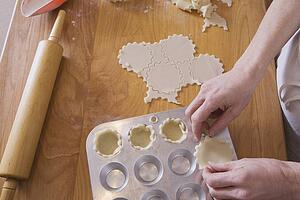 person placing dough into muffin pan on cutting board with rolling pin