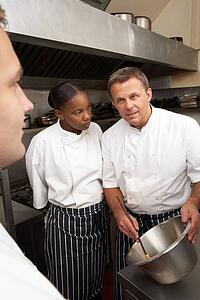 Chef Instructing Trainees In Restaurant Kitchen