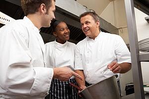 Chef Instructing Trainees In Restaurant Kitchen