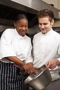 Chef Instructing Trainee In Restaurant Kitchen
