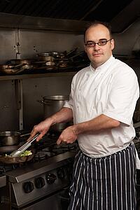 Male Chef Preparing Meal On Cooker In Restaurant Kitchen