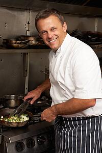 Male Chef Preparing Meal On Cooker In Restaurant Kitchen