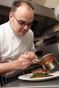 Chef Adding Sauce To Dish In Restaurant Kitchen