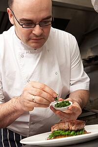 Chef Adding Seasoning To Dish In Restaurant Kitchen