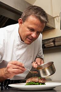 Chef Adding Sauce To Dish In Restaurant Kitchen