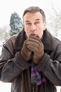 Senior Man Standing Outside In Snowy Landscape Warming Hands