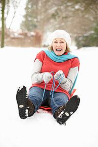 Senior Woman Sledging Through Snowy Woodland