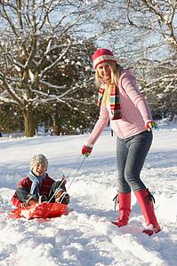 Mother Pulling Son On Sledge Through Snowy Landscape