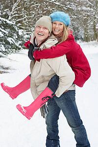 Man Giving Woman Piggyback In Snowy Woodland