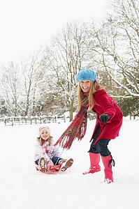 Mother Pulling Daughter On Sledge Through Snowy Landscape