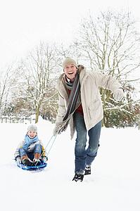 Father Pulling Son On Sledge Through Snowy Landscape