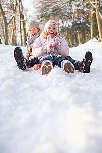 Boy And Girl Sledging Through Snowy Woodland