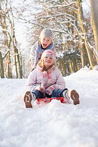 Boy And Girl Sledging Through Snowy Woodland