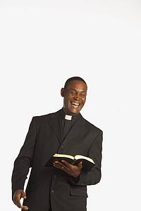 a man wearing a clerical collar and laughing while holding an open bible