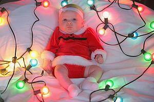 an infant girl in a christmas outfit surrounded by a string of lights