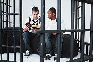 a young man reading the bible to another young man in jail