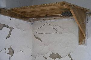 a wooden corner shelf with a hanger mounted on a wall with peeling paint