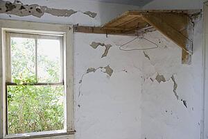 a wooden corner shelf and window along a wall with peeling paint