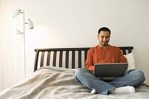 Young Man in Bed Using Laptop