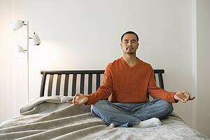 Young Man Meditating in Bedroom