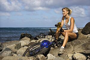 Attractive Young Woman Sitting With Bicycle on Rocky Beach