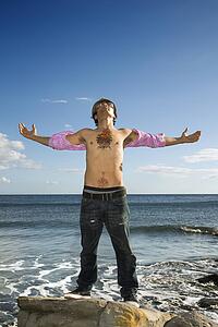 Young Man Standing on Ocean Rock with Arms Outstretched