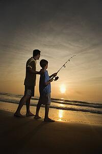 Man and young boy fishing in surf