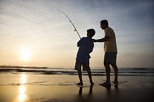 Man and young boy fishing in surf