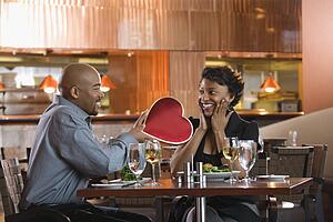Man Giving Woman Heart Shaped Box at Restaurant